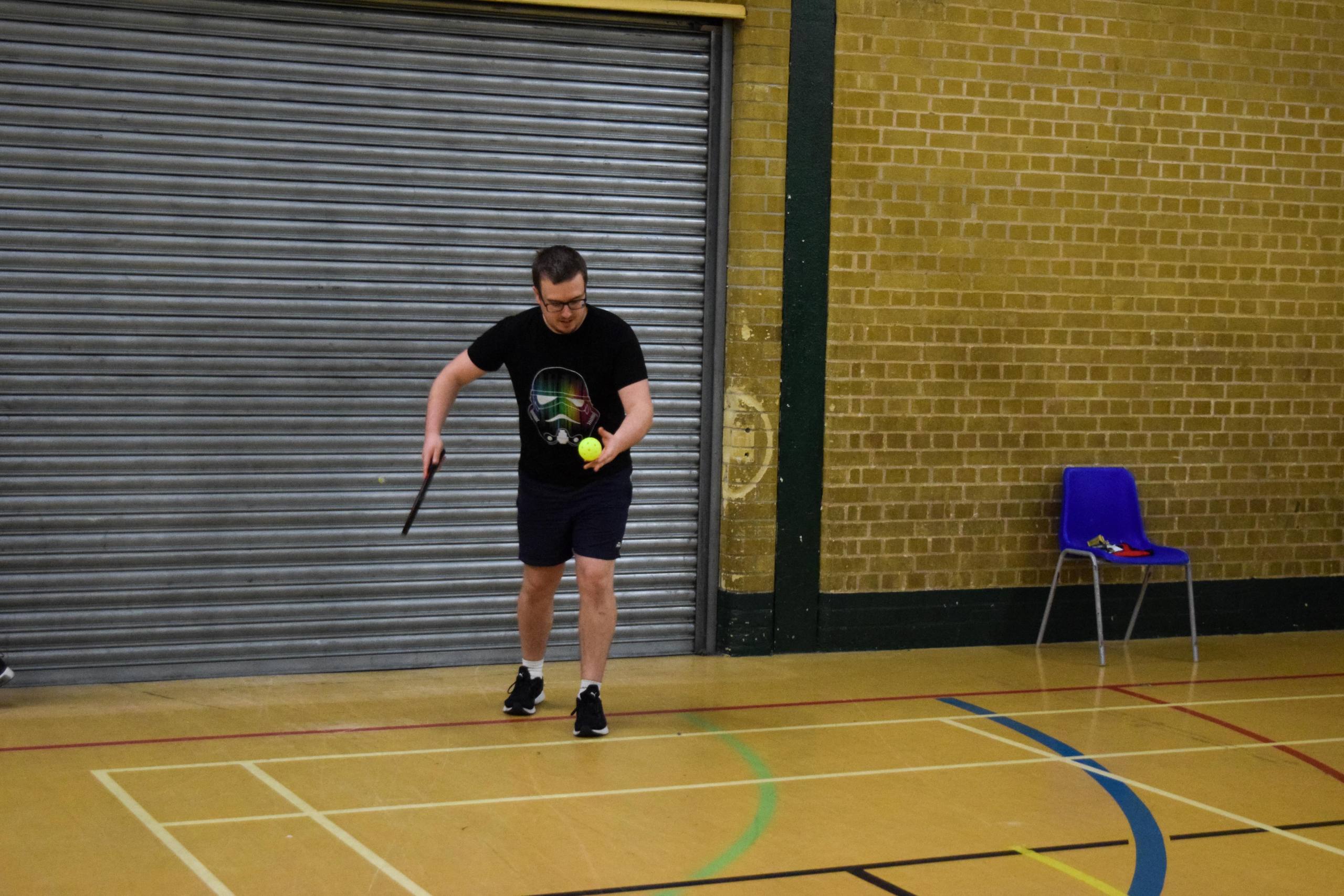 a man holding a pickleball racket and a ball